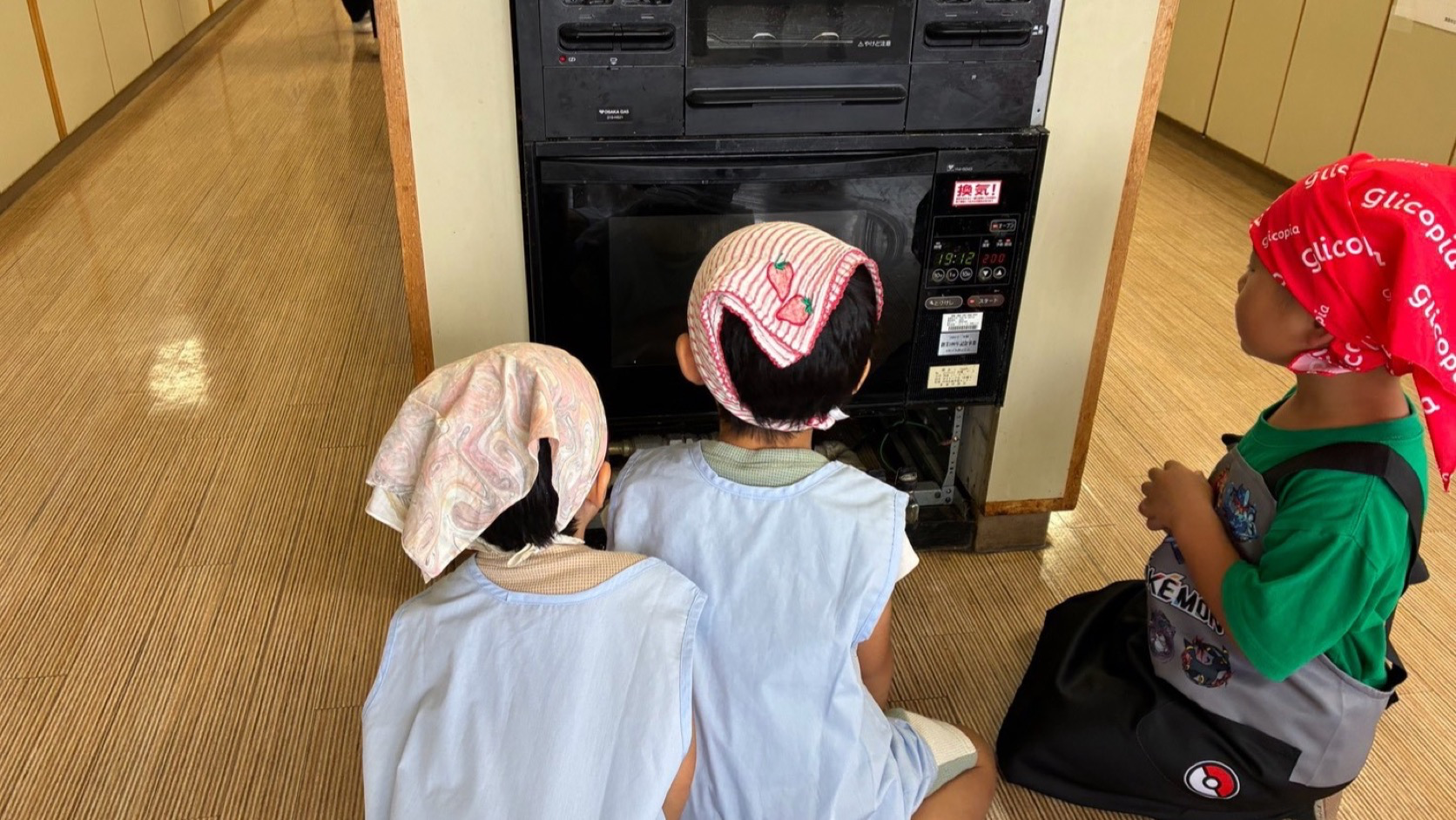 オーブンの前で焼き上がりを観察する子どもたち