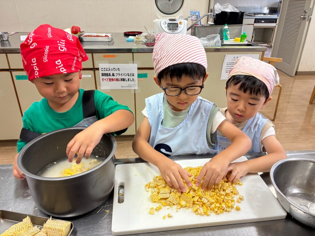 とうもろこしの粒を外し、炊飯釜に入れる作業を分担する子どもたち