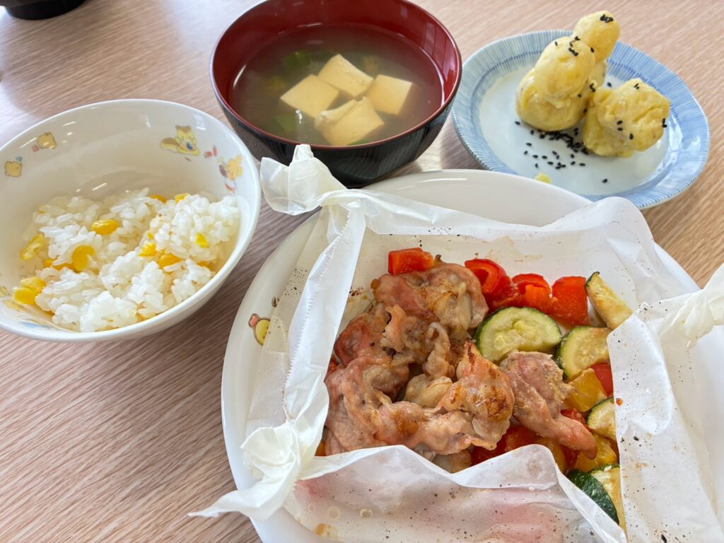 とうもろこしご飯、夏野菜と肉の包み焼き、汁ものなどが並んだ完成料理