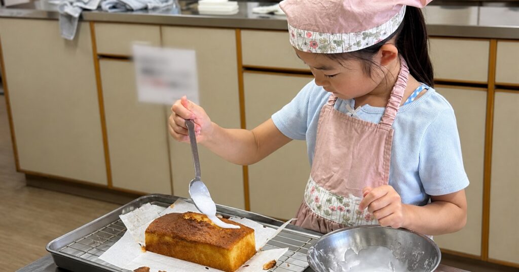 焼きたてのレモンケーキに、スプーンでアイシングをかける子ども