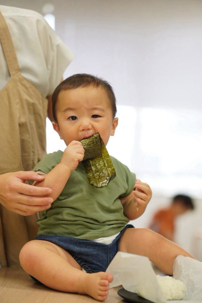 海苔のついたおにぎりを手に持ち、こちらを見る赤ちゃん