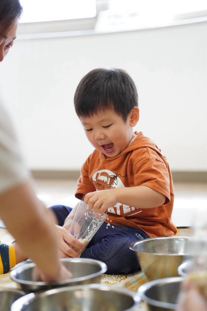 カップからボウルへ雑穀を移し替えて笑う男の子