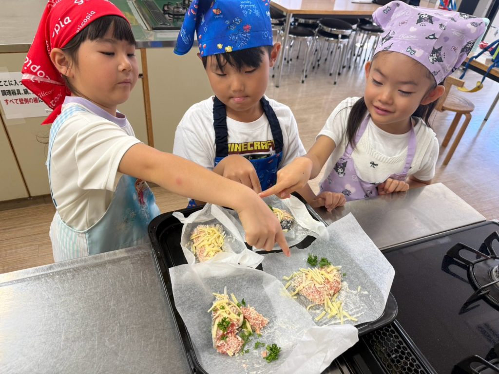 パン粉やチーズをのせた鮭を指さしながら確認する3人の子どもたち