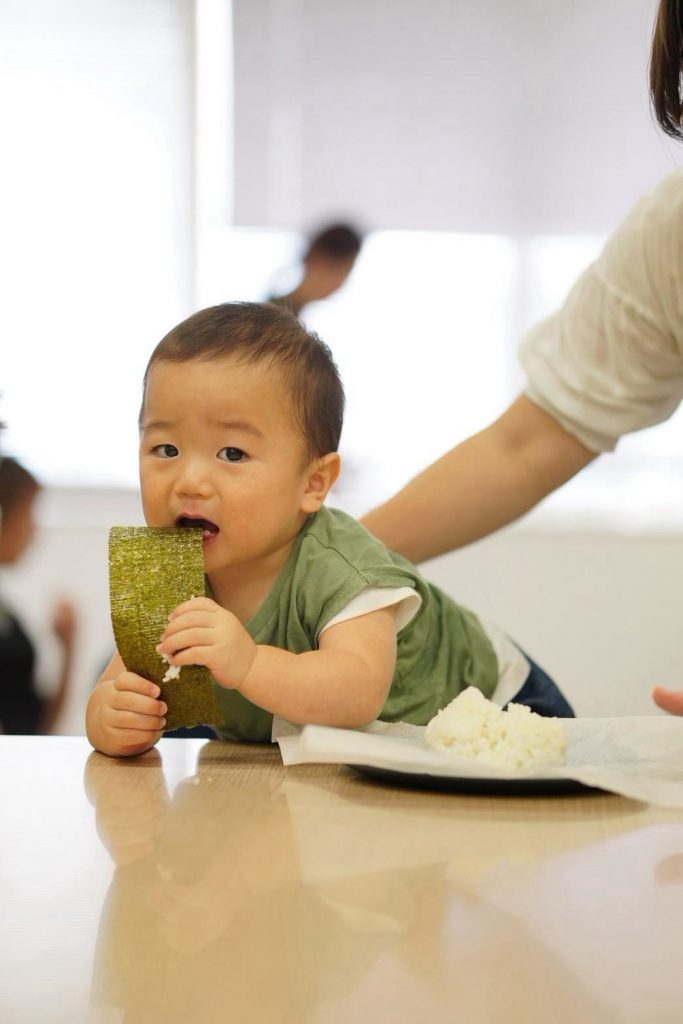 おにぎりを手に持つ赤ちゃんと見守る保護者の手