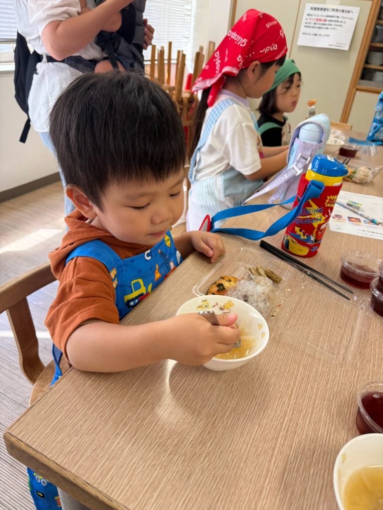 お味噌汁を味わう男の子と、お弁当を食べる周りの子どもたち